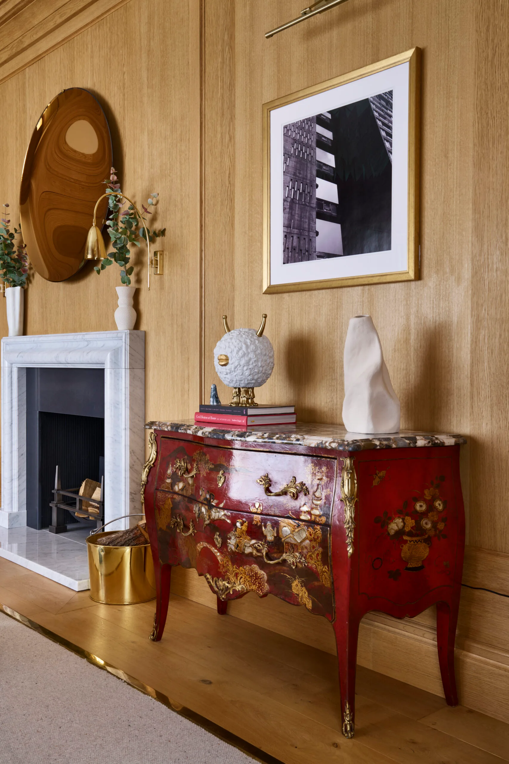 A stylish living room featuring wood-paneled walls, antique chest of drawers, with art books stacked on top and a framed photograph on the wall.