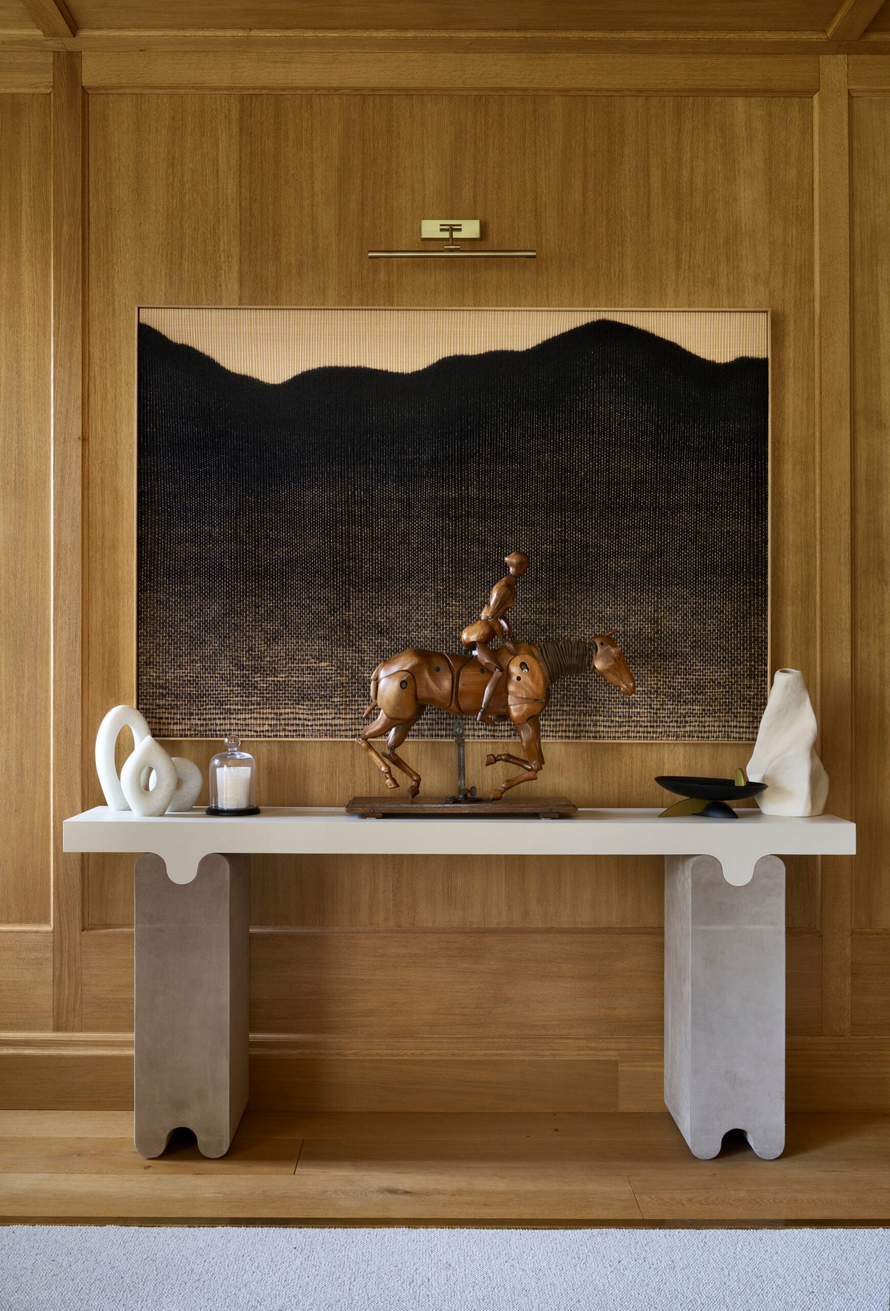 Wooden panelling with artwork centre with console table below with various sculptures and ornaments.